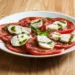 Pomodori a fette con mozzarella, pesto e basilico in un piatto bianco. Immagine generata con intelligenza artificiale