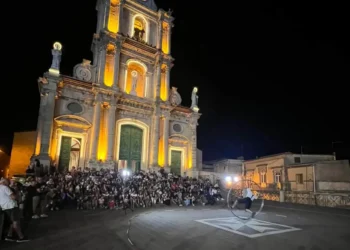 Chiesa di San Giovanni Battista illuminata a Monterosso Almo, pubblico e artista di strada con la ruota durante l'ArtFest