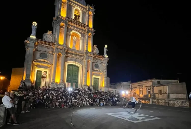 Chiesa di San Giovanni Battista illuminata a Monterosso Almo, pubblico e artista di strada con la ruota durante l'ArtFest