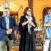 Sul palco di Scacciapensieri a Modica, tre persone con il microfono; una tiene in mano un piatto con una scaccia