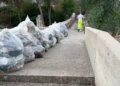 Sacchi di rifiuti allineati sul muretto della scala di San Francesco a Ispica, con un operatore ecologico che sale i gradini