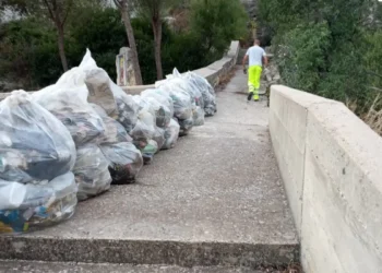 Sacchi di rifiuti allineati sul muretto della scala di San Francesco a Ispica, con un operatore ecologico che sale i gradini