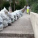 Sacchi di rifiuti allineati sul muretto della scala di San Francesco a Ispica, con un operatore ecologico che sale i gradini