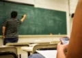 Classe scolastica con insegnante alla lavagna e studente al banco con smartphone