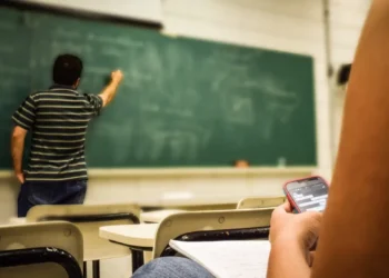 Classe scolastica con insegnante alla lavagna e studente al banco con smartphone