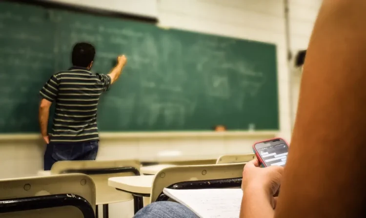 Classe scolastica con insegnante alla lavagna e studente al banco con smartphone