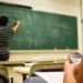 Classe scolastica con insegnante alla lavagna e studente al banco con smartphone