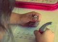 Mano di una bambina che scrive lettere in corsivo su un quaderno a righe con una penna ergonomica