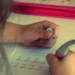 Mano di una bambina che scrive lettere in corsivo su un quaderno a righe con una penna ergonomica