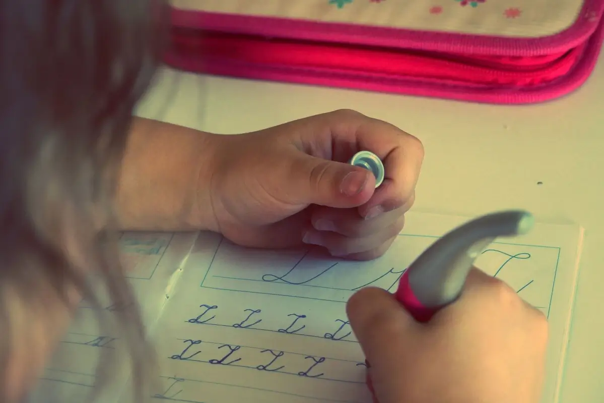 Mano di una bambina che scrive lettere in corsivo su un quaderno a righe con una penna ergonomica