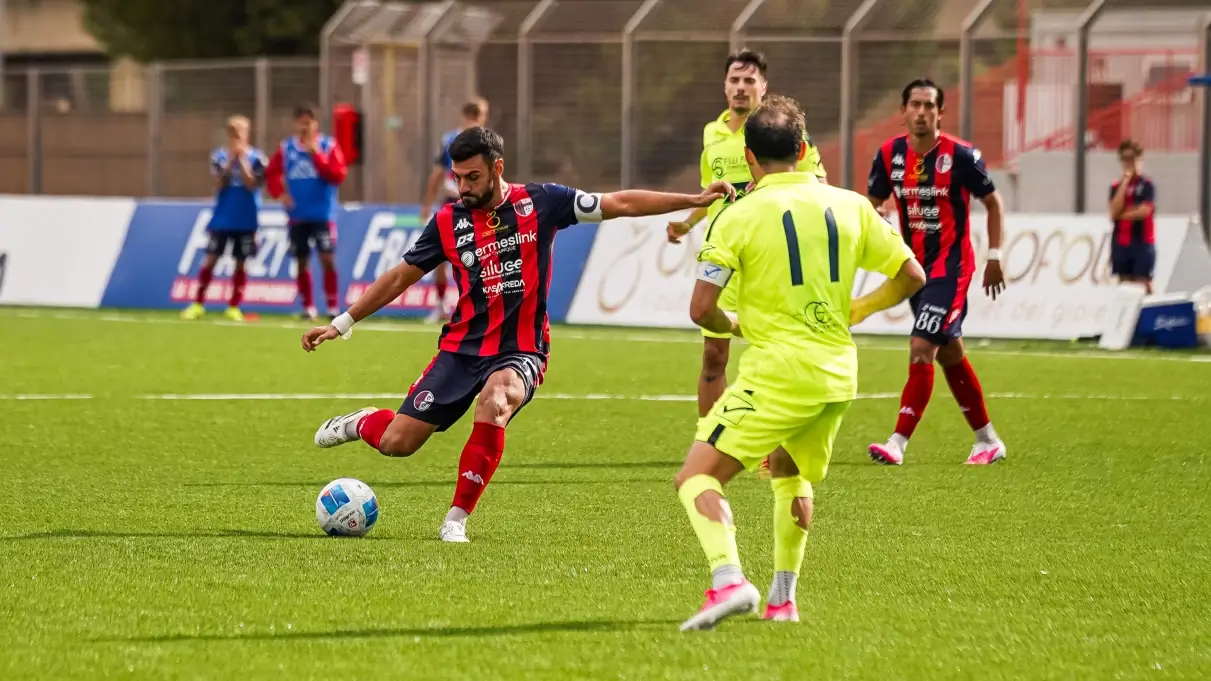Calciatore del Modica in maglia rossoblù con la fascia da capitano calcia il pallone in una gara di Serie D