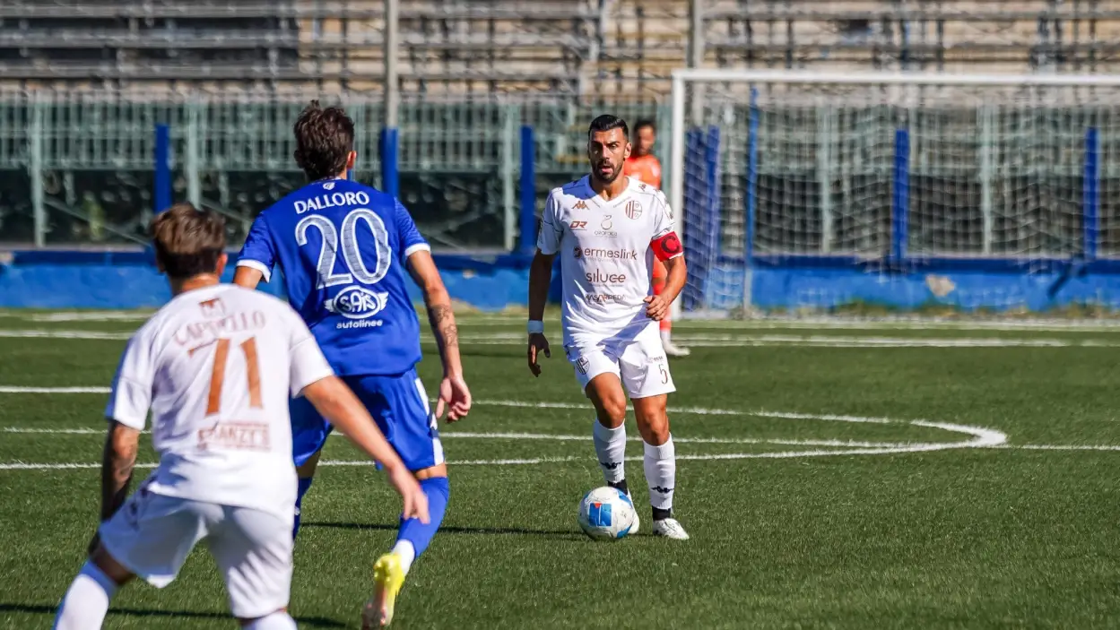 Siracusa-Modica: il capitano in maglia bianca conduce palla a centrocampo, pressato da un avversario in maglia azzurra