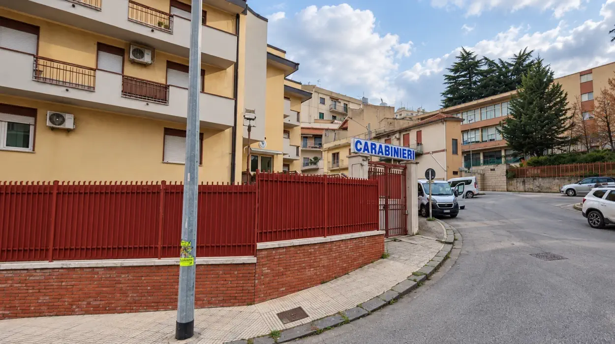 Ingresso della caserma dei carabinieri di San Cataldo, con recinzione e cancello rossi e l'insegna blu
