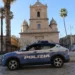 Auto della Polizia di Stato ferma in una piazza siciliana, con chiesa e palme sullo sfondo