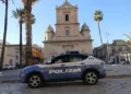 Auto della Polizia di Stato ferma in una piazza di Vittoria, davanti a una chiesa barocca circondata da palme