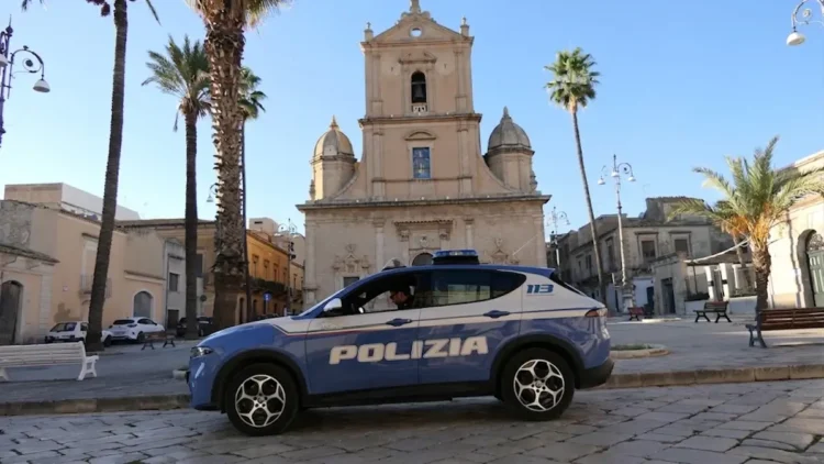 Auto della Polizia di Stato ferma in una piazza di Vittoria, davanti a una chiesa barocca circondata da palme
