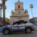 Auto della Polizia di Stato ferma in una piazza di Vittoria, davanti a una chiesa barocca circondata da palme