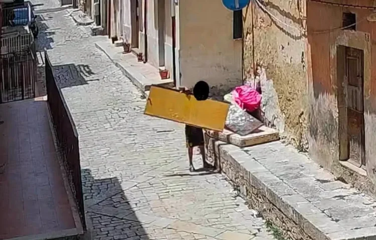 Fotogramma di una telecamera trappola: una persona abbandona un materasso e sacchi di rifiuti lungo una strada