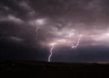 Temporali Sicilia con fulmini illuminano un cielo scuro sopra una zona rurale