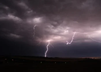 Temporali Sicilia con fulmini illuminano un cielo scuro sopra una zona rurale