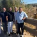 Cinque uomini in piedi lungo un guardrail nei pressi del torrente Trippatore, con un escavatore al lavoro sullo sfondo