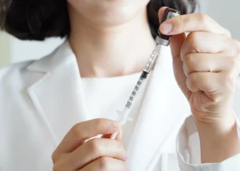Mani di un operatore sanitario in camice bianco preparano una siringa con un vaccino