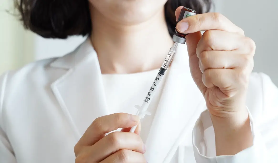 Mani di un operatore sanitario in camice bianco preparano una siringa con un vaccino