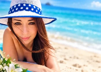 Valeria Costanzo sorride in spiaggia con cappello a righe blu e un mazzo di fiori bianchi tra le mani