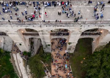 Vista dall'alto del Ponte Vecchio sulla vallata Santa Domenica a Ragusa, con persone sul ponte e nel fondovalle illuminato