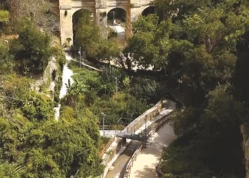 Sentiero con parapetti e lampioni nella Vallata Santa Domenica a Ragusa, tra alberi fitti e un ponte ad arcate in pietra