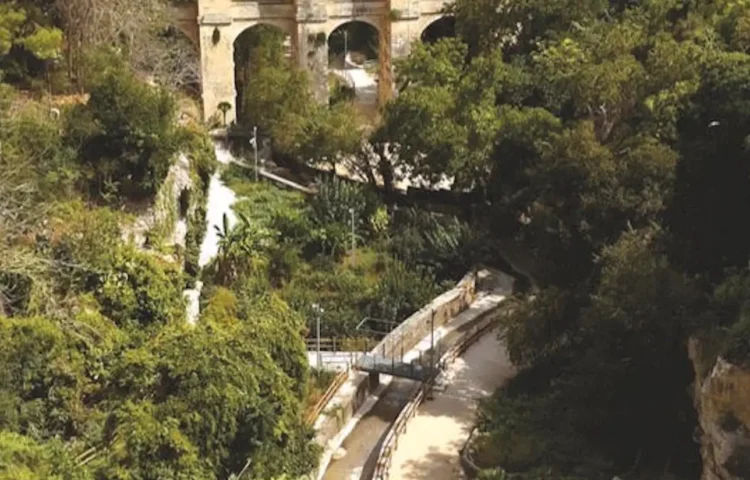 Sentiero con parapetti e lampioni nella Vallata Santa Domenica a Ragusa, tra alberi fitti e un ponte ad arcate in pietra