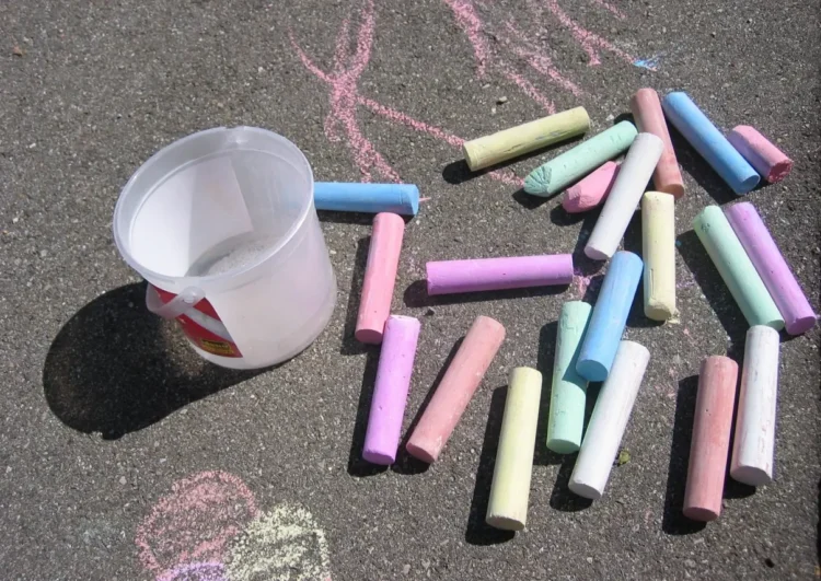 Gessetti colorati e un secchiello di plastica sull'asfalto, con disegni rosa: attività per bambini a Marina di Ragusa