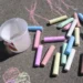 Gessetti colorati e un secchiello di plastica sull'asfalto, con disegni rosa: attività per bambini a Marina di Ragusa