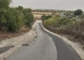 Via 392 a Ragusa, asfalto rattoppato e bordi sterrati tra la vegetazione, sullo sfondo case e traffico