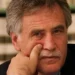Peppe Drago in primo piano, mano vicino al viso, sfondo di una libreria