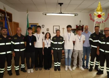 Cinque volontari in gruppo con i vigili del fuoco in divisa, sotto la scritta Vigili del Fuoco, in un ufficio del comando