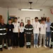 Cinque volontari in gruppo con i vigili del fuoco in divisa, sotto la scritta Vigili del Fuoco, in un ufficio del comando