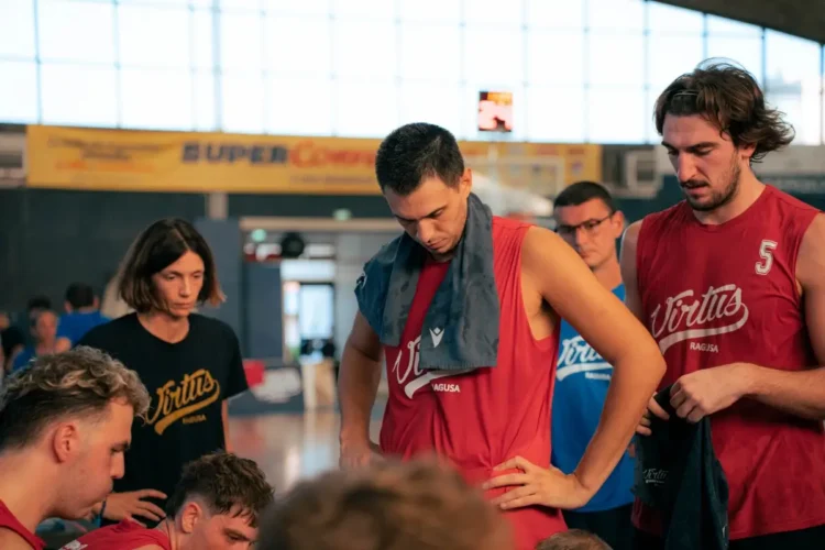 Giocatori della Virtus Ragusa in maglia rossa nello spogliatoio dopo un allenamento, con lo staff tecnico