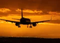 Aereo in fase di atterraggio al tramonto, carrello abbassato contro un cielo arancione