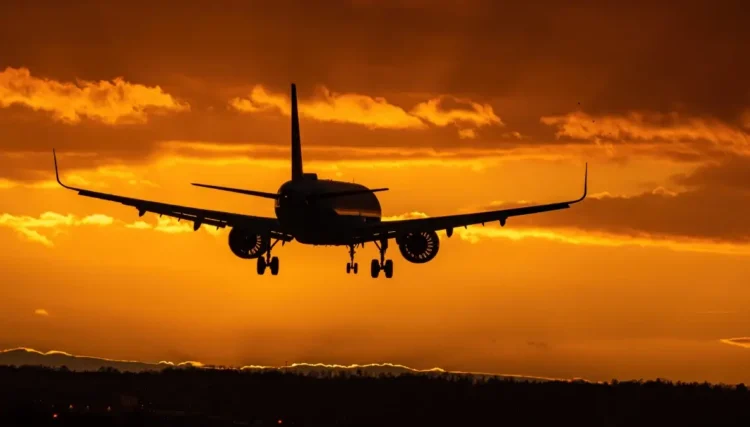 Aereo in fase di atterraggio al tramonto, carrello abbassato contro un cielo arancione