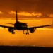 Aereo in fase di atterraggio al tramonto, carrello abbassato contro un cielo arancione