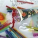 Materiale scolastico colorato: pastelli, pennarelli, forbici, cartoncini e un cono decorato con nastro rosso e tulle bianco