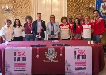 Presentazione della 5K di Vittoria Run & Walk in Comune: undici persone dietro un tavolo con manifesti e medaglie