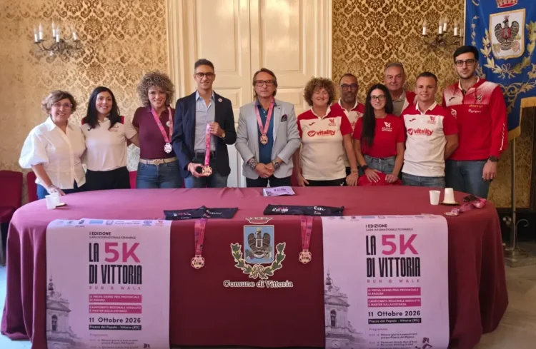 Presentazione della 5K di Vittoria Run & Walk in Comune: undici persone dietro un tavolo con manifesti e medaglie