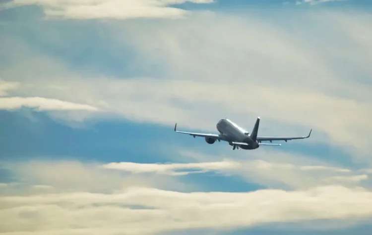 Aereo passeggeri bianco in volo dopo il decollo, con carrello estratto, tra nuvole chiare e cielo azzurro