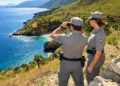 Due agenti del Corpo forestale con binocolo sorvegliano una costa della Sicilia. Immagine generata con intelligenza artificiale