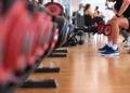Uomo seduto su una panca in palestra con due manubri in mano, accanto a una rastrelliera di pesi per allenare i muscoli