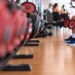 Uomo seduto su una panca in palestra con due manubri in mano, accanto a una rastrelliera di pesi per allenare i muscoli