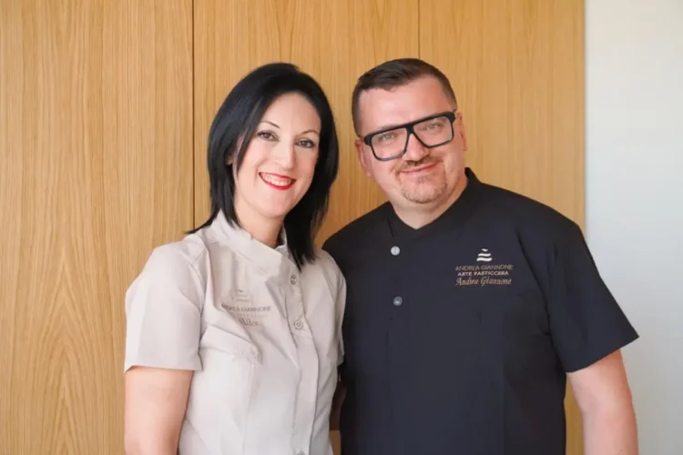 Andrea Giannone e Alice in divisa da pasticceria, sorridenti davanti a una parete rivestita in legno chiaro