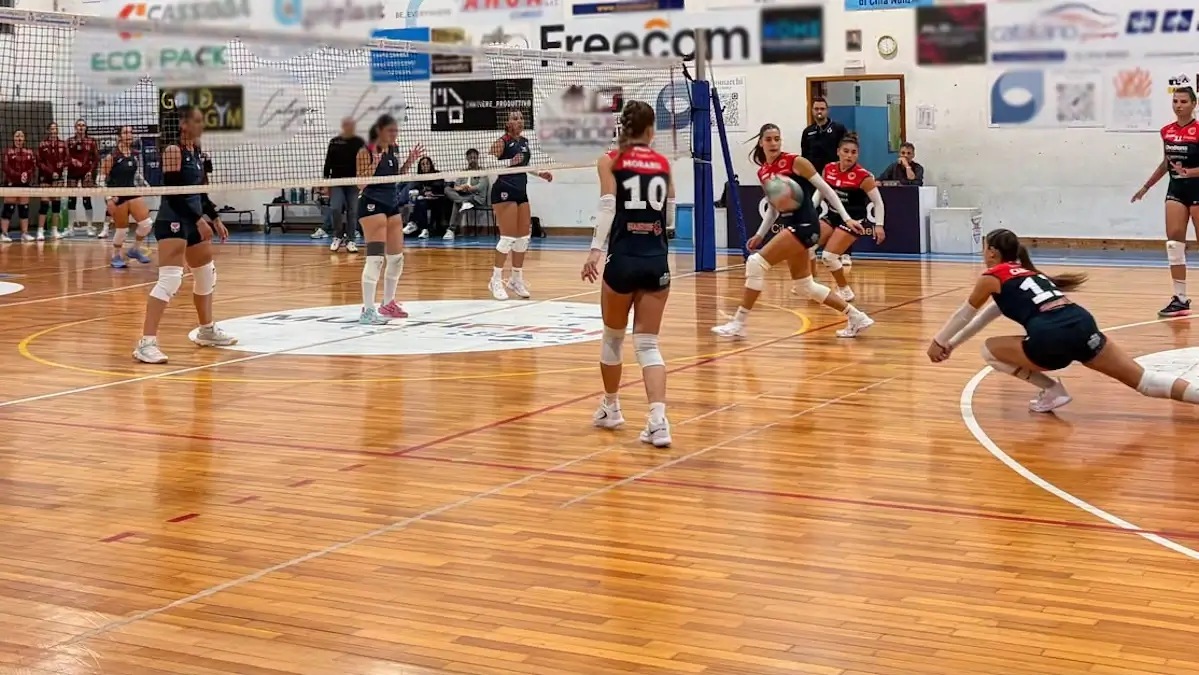 Partita di volley femminile a Comiso: una giocatrice si allunga in bagher per ricevere il pallone, le compagne la guardano